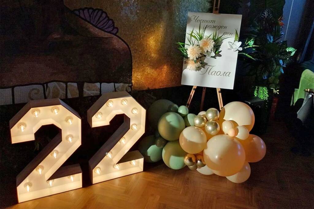 Светещи цифри 22 пред златна стена с балонена декорация